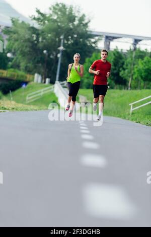 Jeune couple de course à pied sur une route asphaltée dans le parc Banque D'Images