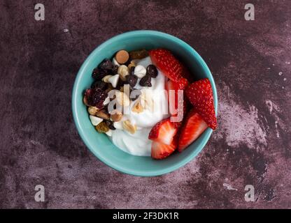 Vue de dessus d'un bol avec yaourt grec ordinaire et un mélange de friandises et des fraises sur une table de marron. Banque D'Images