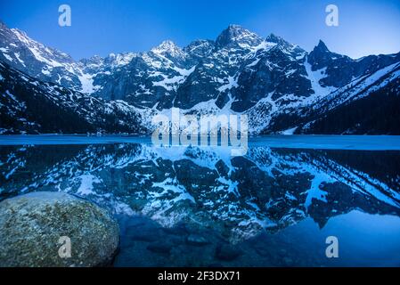 Reflet de pics rocheux brumeux et enneigés dans le lac Eye of the Sea (Morskie oko) en Pologne. Hiver dans les montagnes de Tatra. Banque D'Images