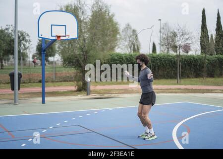 Un athlète énergique dans un entraînement de masque noir sur un terrain de sport avec corde de saut Banque D'Images