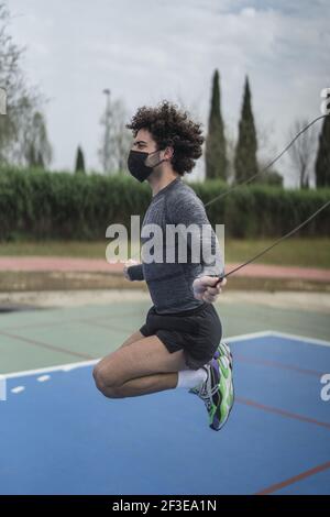 Un jeune espagnol dans un masque noir de formation avec une corde de saut Banque D'Images