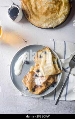Crêpes faites maison, crêpes fines savoureuses avec baies et crème sure sur une assiette grise pour le petit déjeuner sur fond sombre. Cuisine russe traditionnelle. Banque D'Images