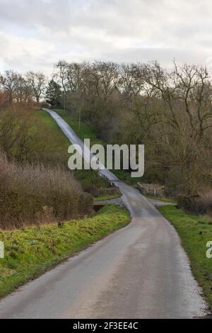 Route de campagne britannique dans la campagne avec haies et herbe de chaque côté, montrant une longue route avec une pente décente et puis monter dans la distance. Banque D'Images