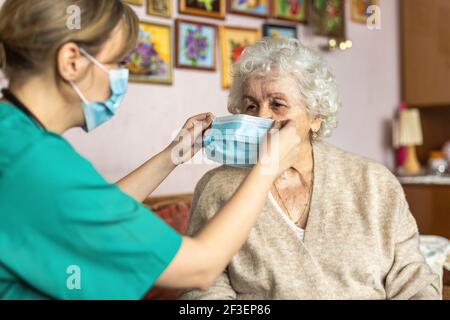 Infirmière féminine aidant une femme âgée à mettre sur la protection masque facial pendant la visite à domicile Banque D'Images