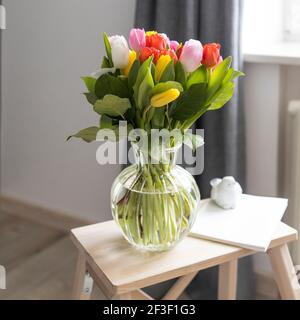 Un bouquet de tulipes multicolores dans un vase transparent sur la chaise haute avec marche sur fond bleu foncé. Ordinateur portable blanc. Banque D'Images