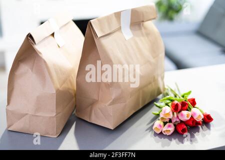 Sacs en papier Kraft avec bouquet de tulipes rouges en fleurs sur fond gris. Fleurs et livraison de nourriture emballage bannière copie espace maquette. Les dons aident Banque D'Images