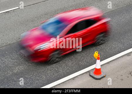 Cône de circulation unique avec lumière fixée sur l'épaule dure d'une autoroute avec une voiture rapide. Vitesse d'obturation lente utilisée pour rendre le mouvement flou. Personne. Banque D'Images