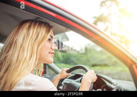 Une femme heureuse et belle conduit une voiture rouge. Banque D'Images