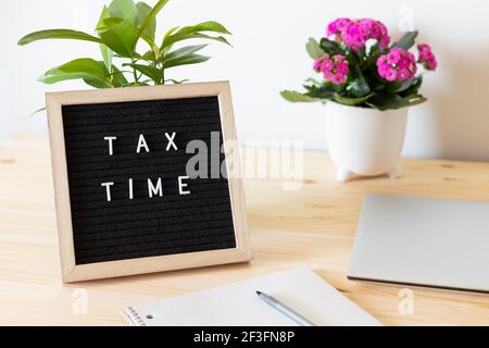 Tableau de lettres en feutre noir, ordinateur portable, bloc-notes et pots de fleurs sur la table. Concept de déclaration de revenus des entreprises. Banque D'Images