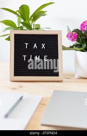 Tableau de lettres en feutre noir, ordinateur portable, bloc-notes et pots de fleurs sur la table. Concept de déclaration de revenus des entreprises. Banque D'Images