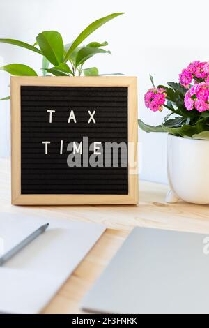 Tableau de lettres en feutre noir, ordinateur portable, bloc-notes et pots de fleurs sur la table. Concept de déclaration de revenus des entreprises. Banque D'Images