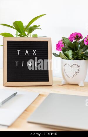 Tableau de lettres en feutre noir, ordinateur portable, bloc-notes et pots de fleurs sur la table. Concept de déclaration de revenus des entreprises. Banque D'Images