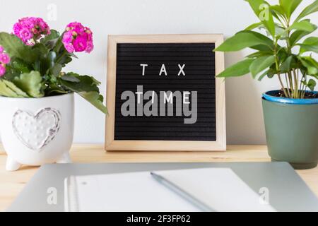 Tableau de lettres en feutre noir, ordinateur portable, bloc-notes et pots de fleurs sur la table. Concept de déclaration de revenus des entreprises. Banque D'Images