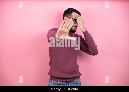 Beau homme portant des lunettes et des vêtements décontractés sur fond rose couvrant les yeux avec les mains et faisant stop geste avec l'expression triste et de peur. EMB Banque D'Images