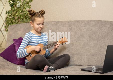 Une adolescente apprend à jouer à l'ukulele et regarde dans son ordinateur portable. Banque D'Images