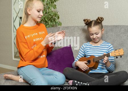 Deux sœurs assises au rez-de-chaussée, jouent ukulele avec le sentiment intéressé, faisant de l'activité ensemble. Banque D'Images