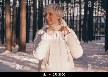 Portrait d'une heureuse femme d'âge moyen dans un parc municipal enneigé au coucher du soleil. Sourit et regarde. Vacances d'hiver et concept de voyage. Banque D'Images