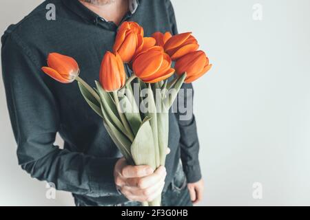 Un homme tient un bouquet de fleurs devant lui. Tulipes orange vif comme cadeau pour l'anniversaire, la Saint-Valentin, la Fête des mères, la Journée internationale de la femme. Banque D'Images