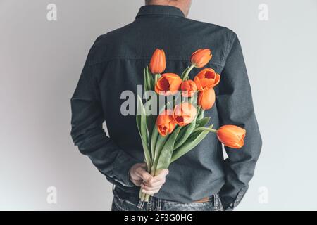 Beau homme avec un bouquet de tulipes orange derrière son dos. Surprise pour votre femme bien-aimée. Concept de vacances romantiques. Saint-Valentin, Fête des mères Banque D'Images