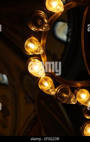 Lampes en verre dans un lustre circulaire en bronze émanant chaud lumière dans l'obscurité devant un dôme de mosquée Banque D'Images