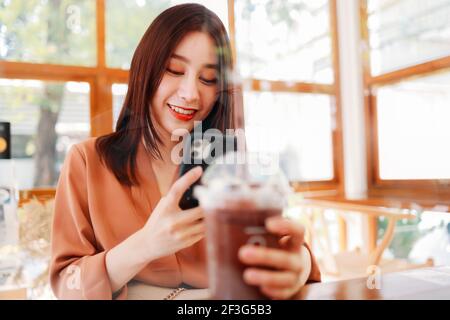 Souriant belle jeune asiatique femme blogueur de nourriture tenant une prise retirez le verre de tremblement et de smoothie pendant que vous prenez des photos téléphone Banque D'Images