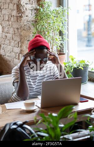 Travailleur indépendant noir concentré regardant un webinaire éducatif sur ordinateur portable, travaillant en ligne à distance dans un café Banque D'Images