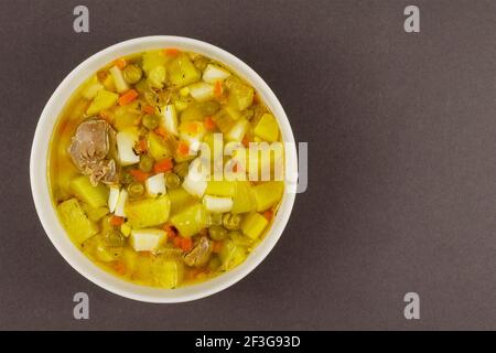 Soupe de poulet aux légumes dans un bol en céramique blanc sur fond gris. Gésiers de poulet, pois, œufs de poulet, pommes de terre, oignons, carottes, herbes. Haut Banque D'Images