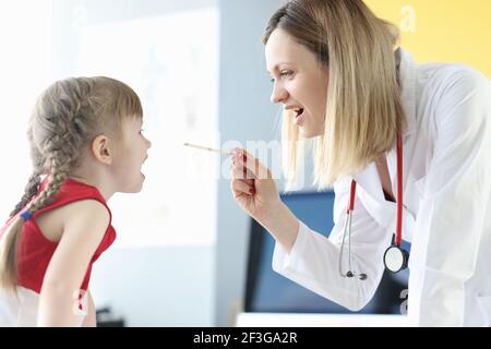 Femme médecin examinant la gorge de la petite fille avec la spatule dedans clinique Banque D'Images