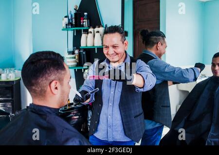 latin homme styliste couper les cheveux à un client dans un salon de coiffure au Mexique Banque D'Images