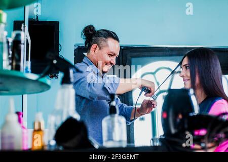 latin homme travaillant comme coiffeur et coupant les cheveux de une femme dans un salon de beauté petite entreprise à Mexico Banque D'Images