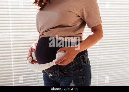 Les mains de la jeune femme enceinte mettent des écouteurs avec de la musique classique sur son ventre. Concept de développement intra-utérin intellectuel de l'enfant Banque D'Images