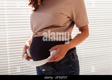 Les mains de la jeune femme enceinte mettent des écouteurs avec de la musique classique sur son ventre. Concept de développement intra-utérin intellectuel de l'enfant Banque D'Images