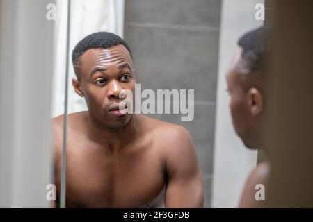 Un jeune homme afro-américain, beau et regardant lui-même dans le miroir Banque D'Images