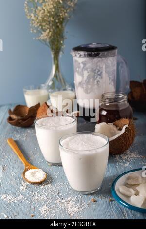 Verre de smoothies à la noix de coco. Smoothie à la noix de coco en tranches de noix de coco fraîches et flocons dans une cuillère sur fond de bois. Banque D'Images