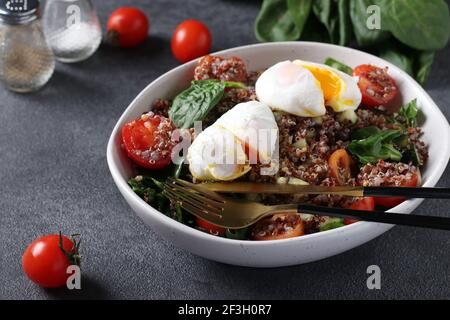 Dans une assiette de quinoa, d'épinards, d'œufs pochés, de concombres et de tomates cerises sur fond gris. Une alimentation saine. Banque D'Images