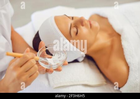 Mains de cosmétologue mélange masque hydratant avec brosse à appliquer sur le visage des jeunes femmes Banque D'Images