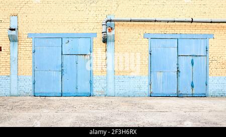 Paysage urbain. Vue symétrique urbaine de l'usine abandonnée bâtiment bleu peint deux portes rouillées sur mur de brique jaune avec lanterne antidéflagrante et Banque D'Images