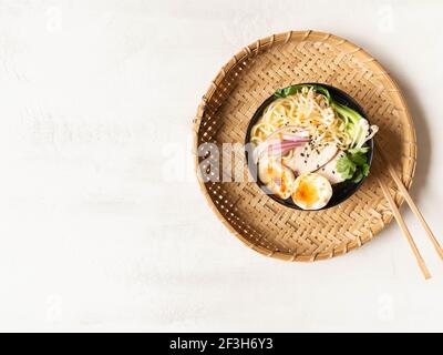 Soupe de nouilles ramen de poulet avec viande, bok choy, champignons, œuf dans un bol noir sur fond gris. Vue de dessus. Espace de copie Banque D'Images