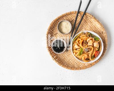 Nouilles Udon avec fruits de mer et légumes cuits dans un wok dans un bol blanc sur un plateau en osier. Vue sur le dessus. Copier l'espace Banque D'Images