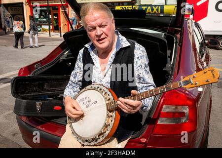 Le chauffeur de taxi irlandais est assis dans le coffre de sa voiture et joue un banjo en attendant les tarifs à la station de taxi de College Street à Killarney, dans le comté de Kerry, en Irlande Banque D'Images
