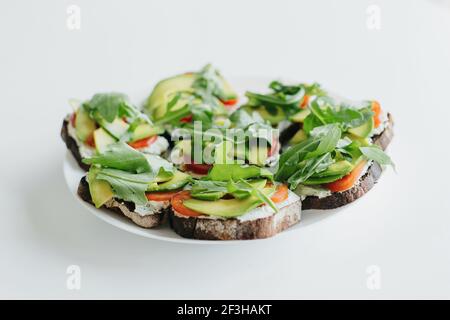 Pain grillé à l'avocat maison sur une assiette sur un comptoir blanc dans une cuisine moderne. Sandwich composé de pain aux grains entiers, d'avocat, de tomate, d'arugula et de fromage. Santé Banque D'Images