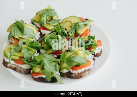 Pain grillé à l'avocat maison sur une assiette sur un comptoir blanc dans une cuisine moderne. Sandwich composé de pain aux grains entiers, d'avocat, de tomate, d'arugula et de fromage. Santé Banque D'Images