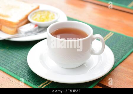 Thé chaud dans une tasse blanche avec pain grillé sur la table comme petit déjeuner Banque D'Images