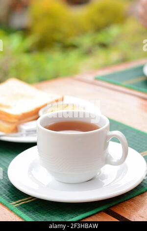 Thé chaud dans une tasse blanche avec pain grillé sur la table comme petit déjeuner Banque D'Images