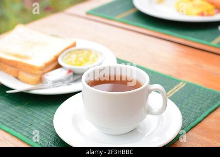 Thé chaud dans une tasse blanche avec pain grillé sur la table comme petit déjeuner Banque D'Images