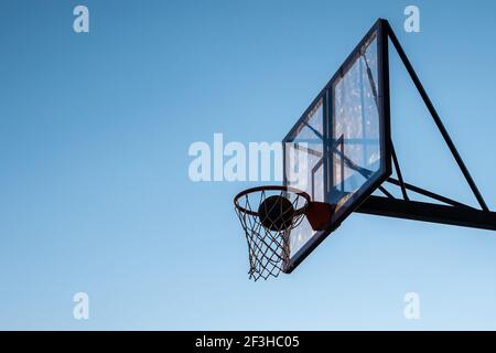 Un basket-ball dans un panier contre un ciel bleu. Banque D'Images