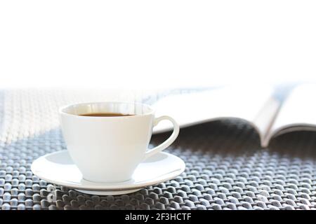 Tasse à café avec livre sur table en osier brun Banque D'Images