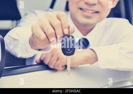 Homme souriant donnant la clé de la voiture tout en étant assis dans la voiture, assurance automobile, vente et location de concepts - style vintage (rétro) effet de couleur Banque D'Images