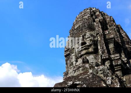 Face en pierre souriante de près avec fond bleu ciel au temple Khmer Prasat Bayon à Angkor, Cambodge Banque D'Images