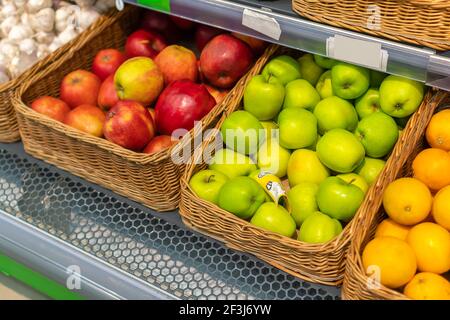 Gros plan de pommes vertes et rouges fraîches, oranges dans des paniers en osier sur le comptoir du magasin Banque D'Images